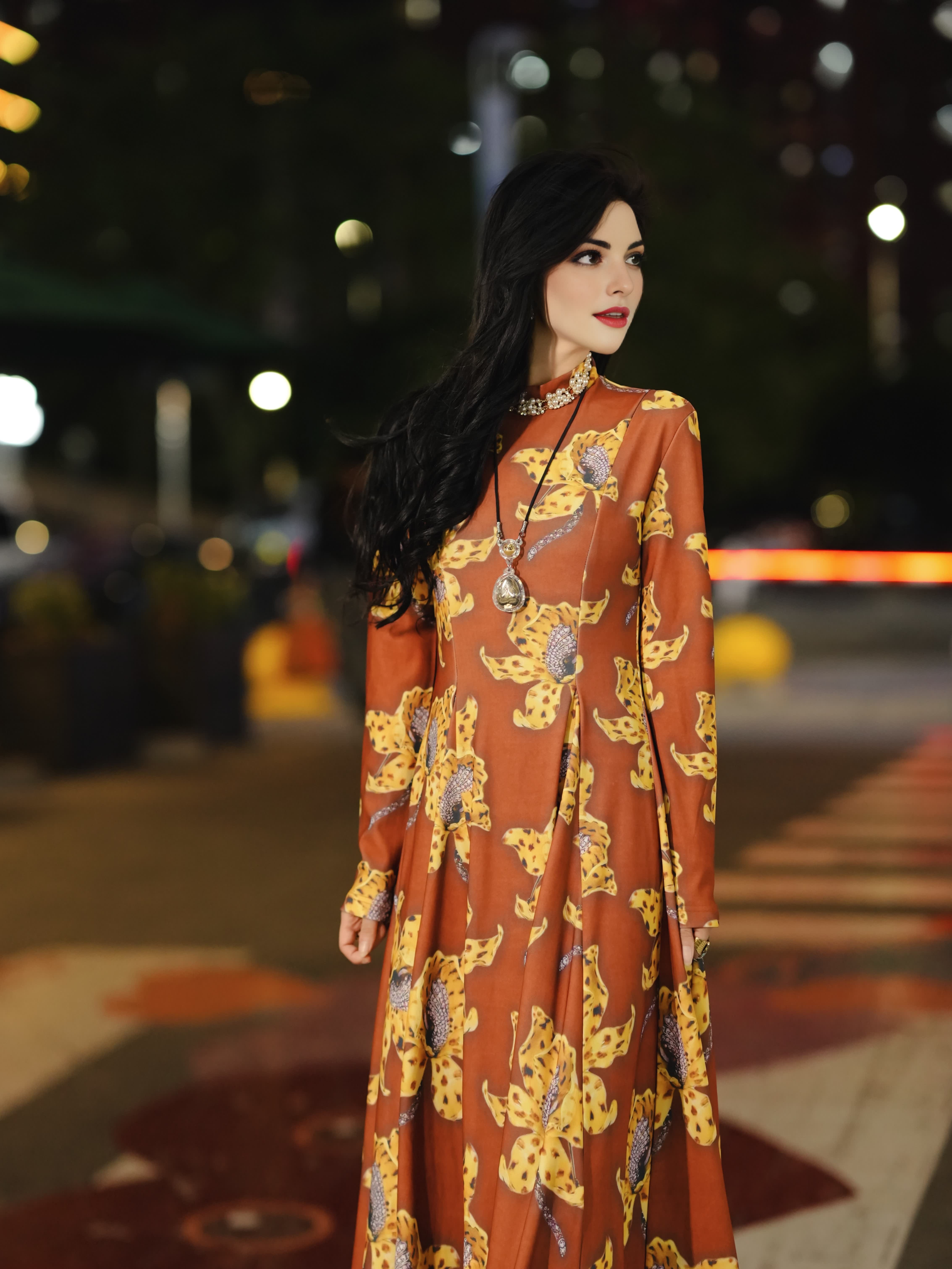 New designer dress features a brown color with a yellow floral print, long sleeves, and a flattering, fitted silhouette; it exudes elegance and a touc