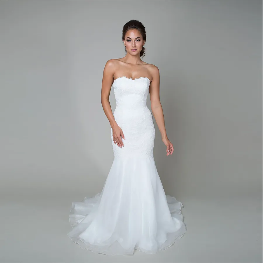La robe de mariée de style trompette comprend une taille basse, un décolleté en cœur, une jupe fluide en organza et une robe de mariée en dentelle avec cordon