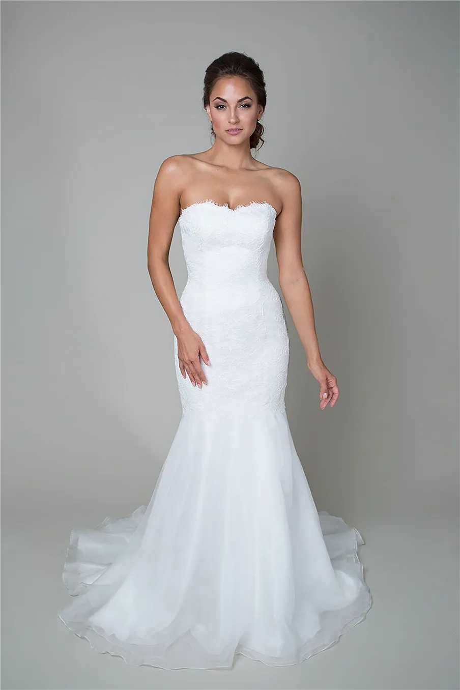 La robe de mariée de style trompette comprend une taille basse, un décolleté en cœur, une jupe fluide en organza et une robe de mariée en dentelle avec cordon