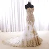 Abiti da sposa con applicazioni di pizzo in vero oro e strascico di corte. Abito da sposa elegante a sirena con lacci e cintura